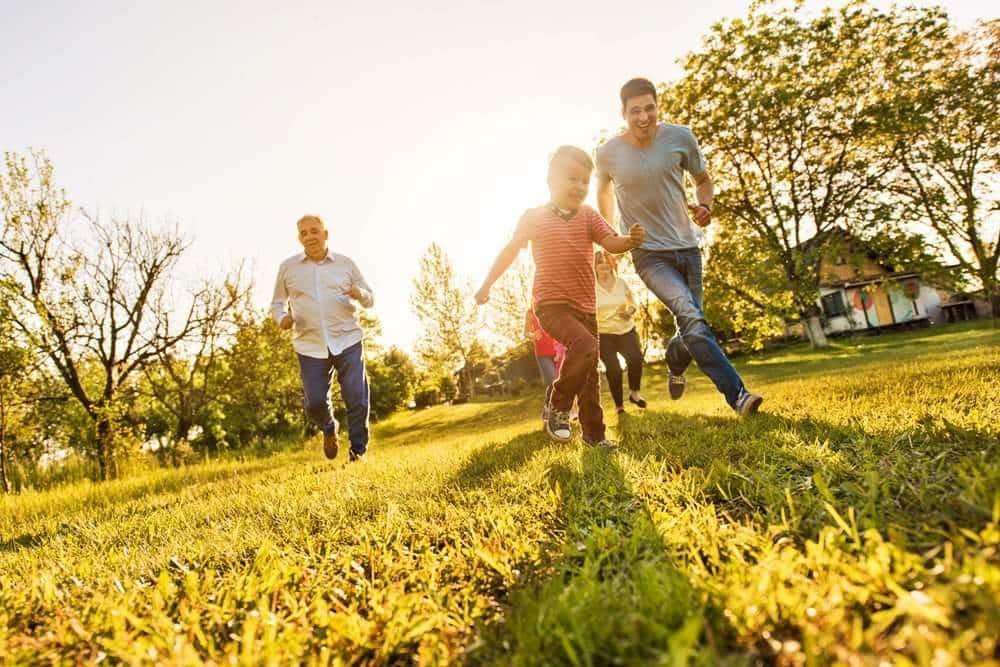 Cheerful little boy running on the grass with his family